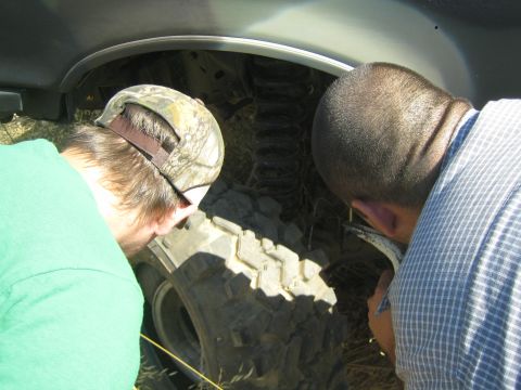 1990 Ford Bronco - Two men lean in to closely examine the aggressive tread of a truck's large off-road tire inside the wheel well.