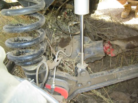 1990 Ford Bronco - Underbody view of a lifted truck's front suspension showing a coil spring, shock absorber and steering components over dirt.