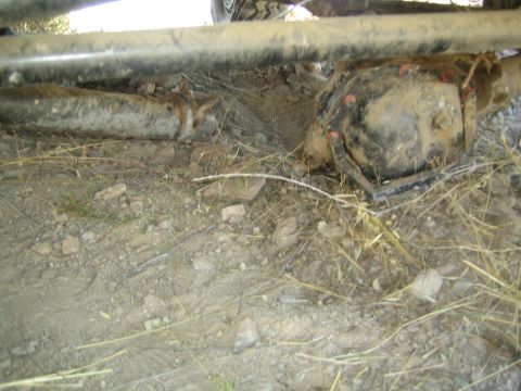 1990 Ford Bronco - Ground-level view of a 4x4's rusty solid front axle and differential housing with red-capped bolts in dry dirt.
