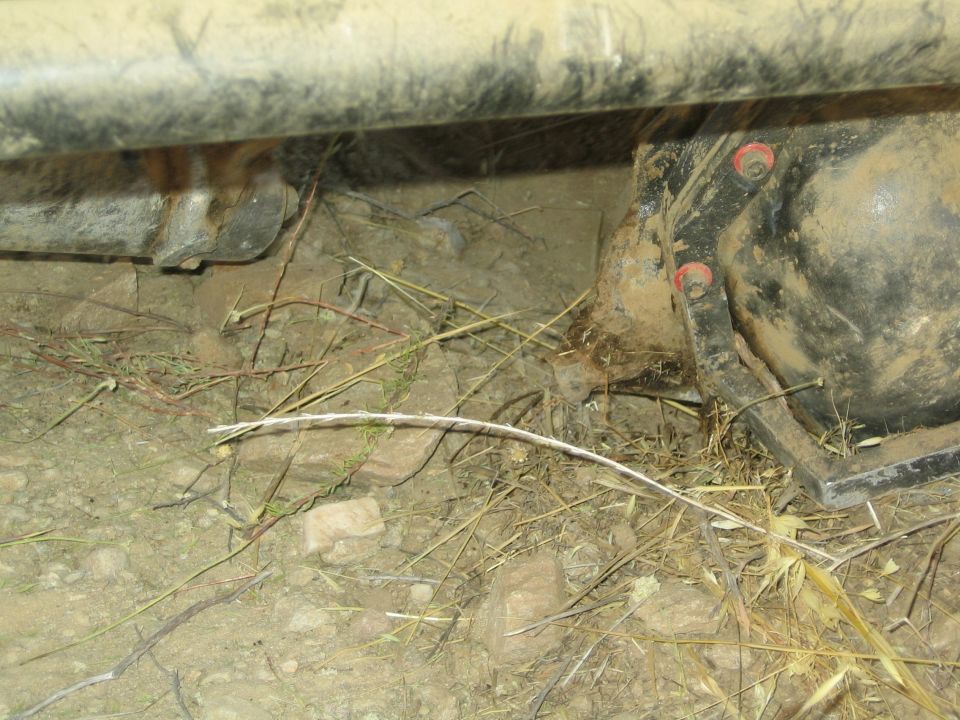 Underside of a vehicle showing axle housing, leaf spring shackle and wiring in dirt
