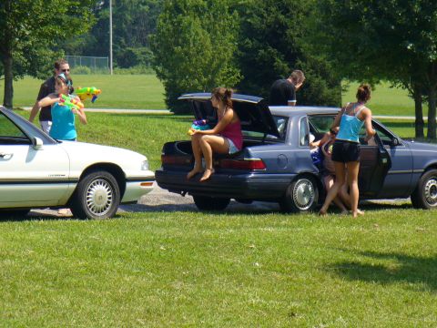 1991 Ford Probe - People are gathered around two cars on a sunny day, some holding water guns.