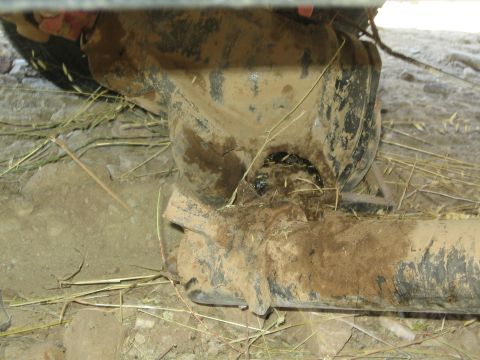 1990 Ford Bronco - Mud-caked underbody of a 4x4 showing the axle tube, U-bolts and pinion area surrounded by dry straw and dirt.