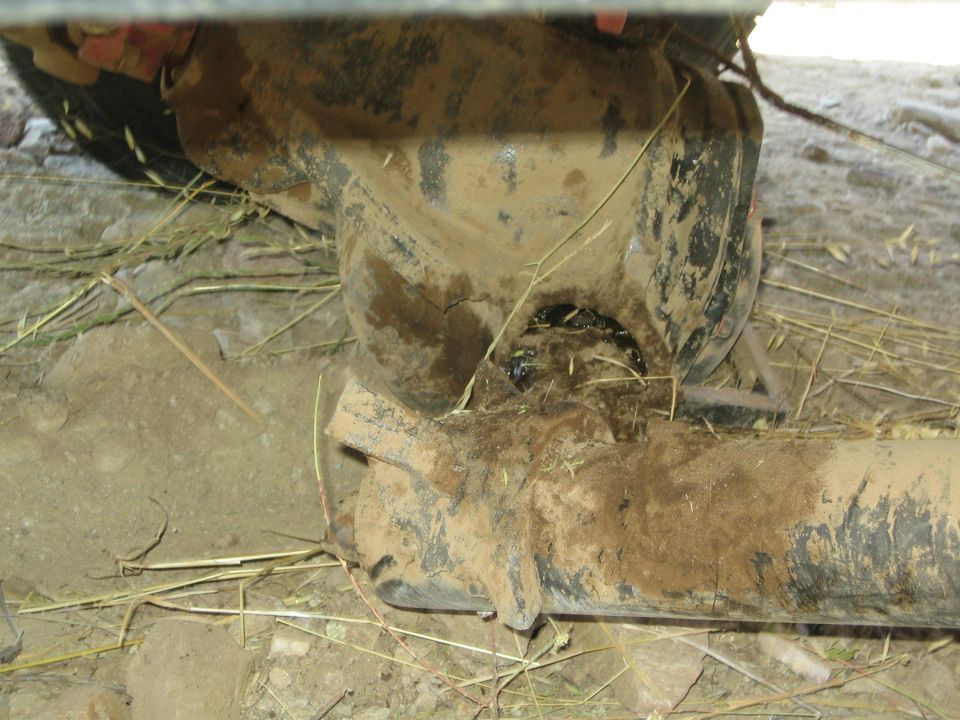 Muddy underside of a vehicle showing axle tube, U-bolts and pinion in dirt