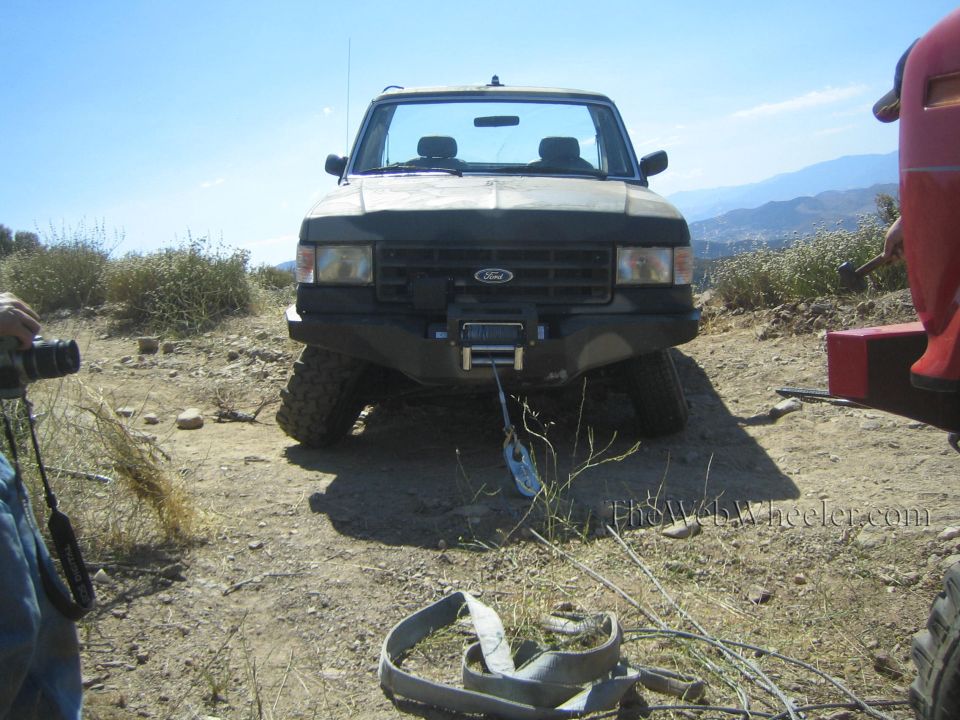 Front view of a lifted Ford pickup with winch on big tires, on a dirt hill