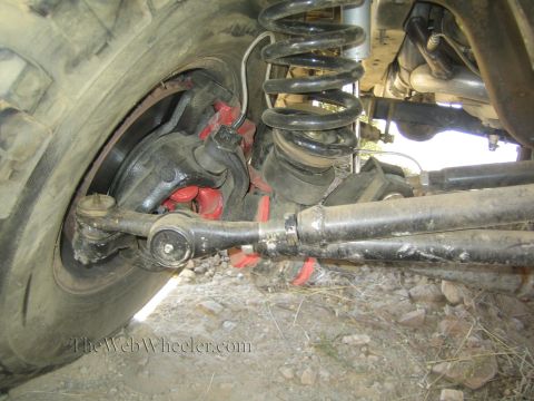 1990 Ford Bronco - Close-up of a 4x4's front suspension with a red-painted control arm, black coil spring, tie rod and oversized tire.