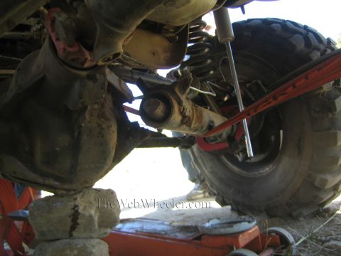 1990 Ford Bronco - Under a lifted 4x4: the front axle stub, knuckle and U-joint exposed with an orange recovery strap and big tire alongside.