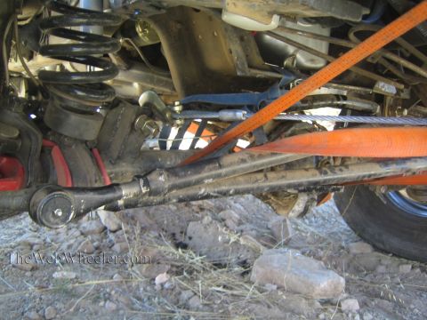 1990 Ford Bronco - Underbody close-up of a 4x4 front suspension with coil spring, tie rod, a steel cable and an orange recovery strap.