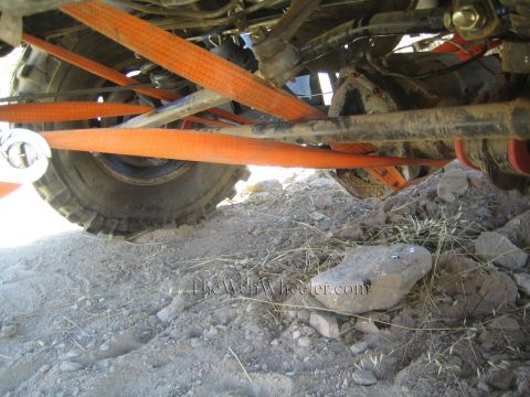 1990 Ford Bronco - Underbody view of a 4x4 with orange recovery straps crossing over a tire and axle, a large rock on the ground beneath.