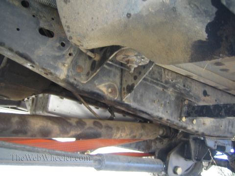 1990 Ford Bronco - Underbody view of a vehicle showing the frame rails, crossmember, driveshaft and exhaust with an orange strap below.