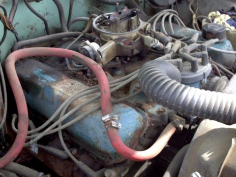 1965 Ford F-100 - Close-up view of a rusty engine bay with various hoses and engine components visible.