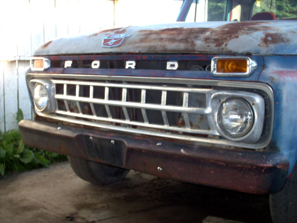 Front view of a rusty 1965 Ford F-100 truck grille and hood emblem