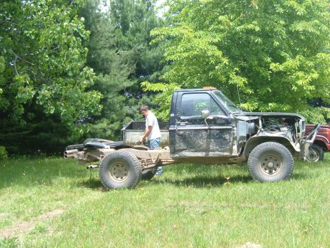1985 Ford F-150 - A black pickup truck chassis with its cab intact is parked on a grassy area, with a person working on it.
