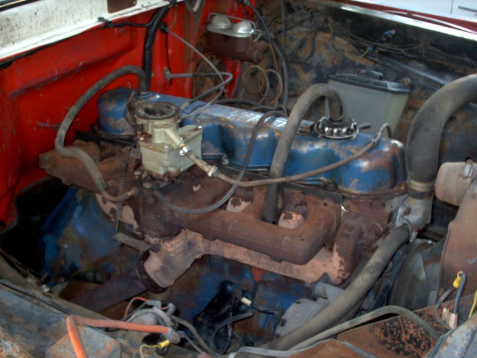 Engine bay with blue valve covers, carburetor, and rusty exhaust manifolds