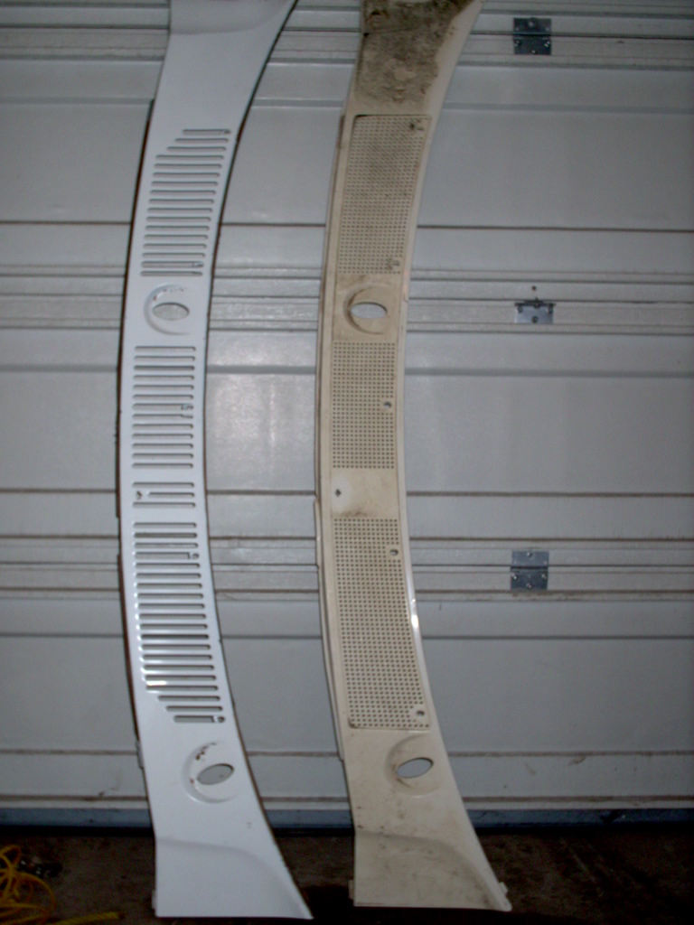 Two curved automotive trim panels, one clean white and one yellowed, leaning against a garage door.