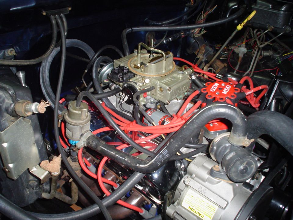 V8 engine bay with gold four-barrel carburetor, red MSD plug wires and red distributor cap