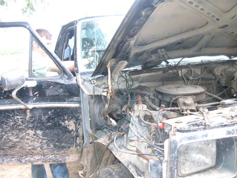 1985 Ford F-150 - Muddy truck with engine exposed, driver's side door open. Likely an older Ford model.