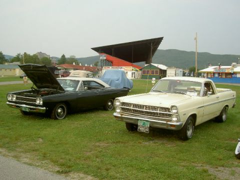 1967 Ford Ranchero - A cream 1967 Ford Ranchero is parked on grass next to a black car with its hood up.