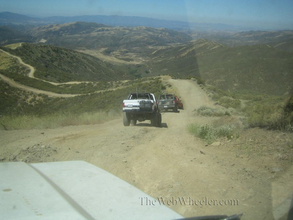 View over a truck hood of two trucks descending a winding hillside dirt road