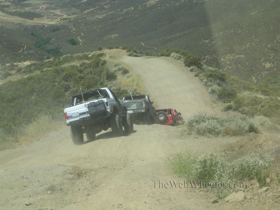 White lifted truck towing a strap toward a vehicle stuck at edge of dirt road