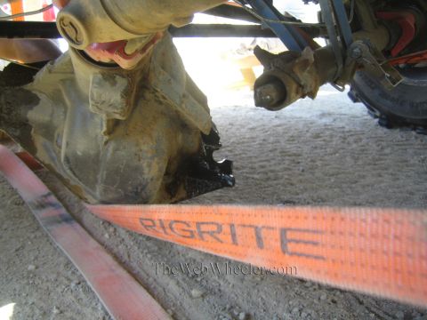 1990 Ford Bronco - Underbody close-up of a leaking axle and driveshaft dripping dark fluid onto sand above an orange RIGRITE recovery strap.