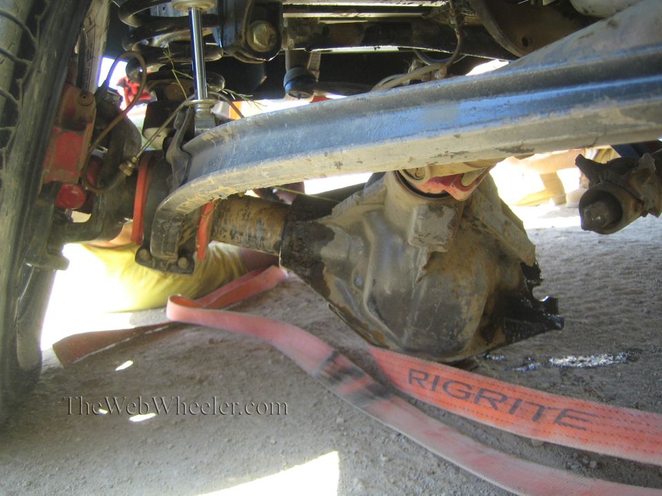 Underside view of a vehicle's front axle, leaf spring and orange recovery strap