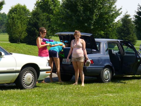 1991 Ford Probe - People are gathered around the back of a blue sedan, some with water guns, on a sunny day.