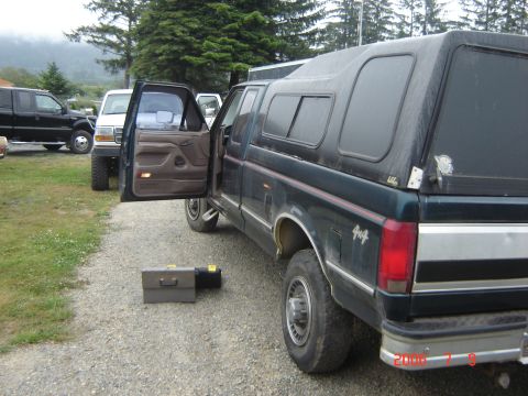 1993 Ford Bronco - A dark green pickup truck with a camper shell and a 4x4 badge is parked on a gravel lot.