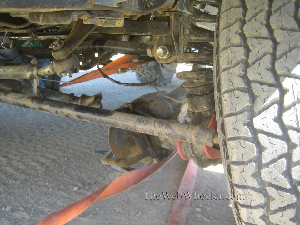 Underside of a lifted 4x4 showing axle, steering linkage and large tire