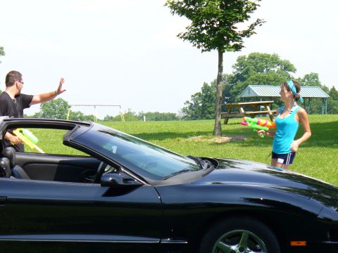 1991 Ford Probe - A black convertible sports car is parked on a grassy field with two people holding water guns.