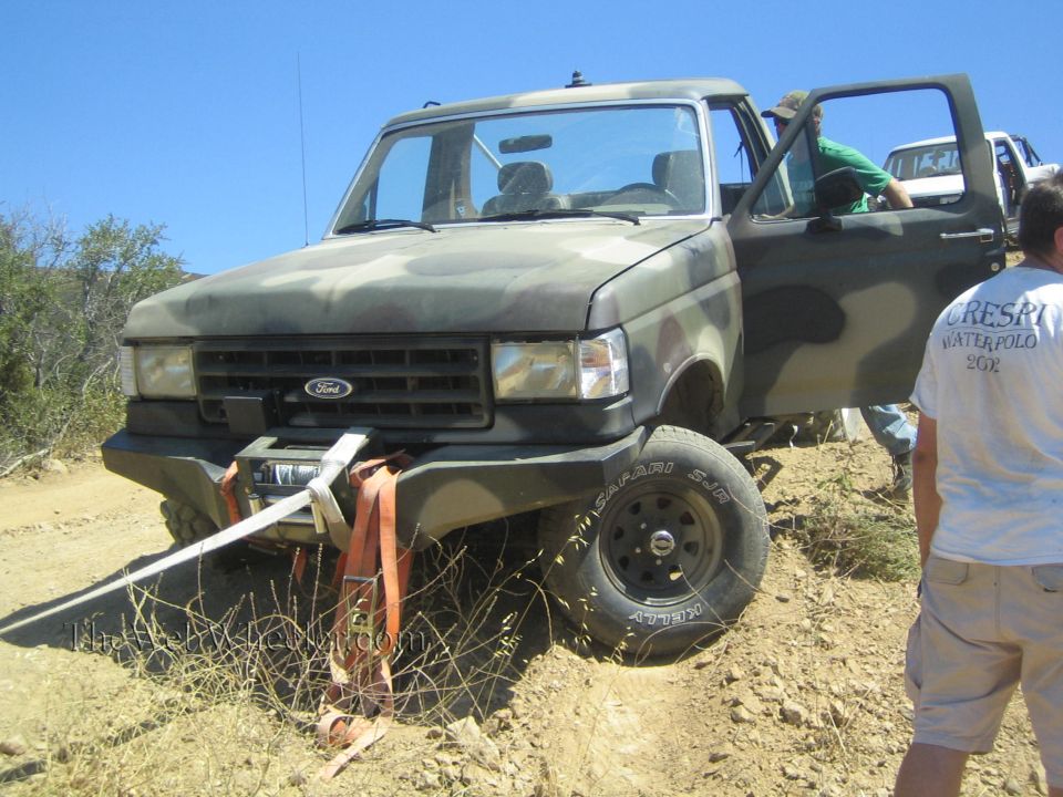 Camo Ford 4x4 with open doors and winch line, people standing alongside