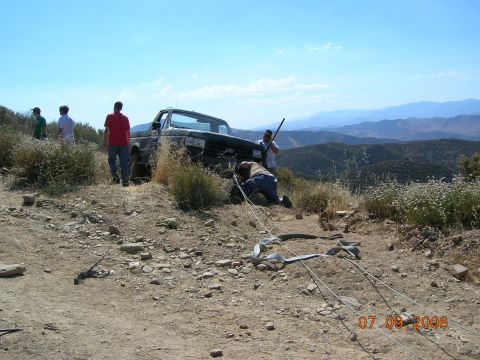 1985 Ford Bronco - People winching a stuck Ford Bronco on a steep, rocky hill with mountains in the distance.