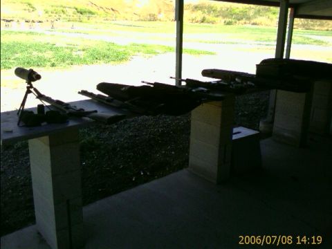 1990 Ford Bronco - Rifles are lined up on a table at a shooting range, with a spotting scope to the left.