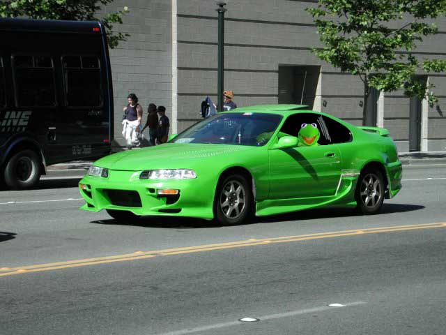 Bright green Honda Prelude with body kit on a city street, Kermit the Frog plush in the passenger window