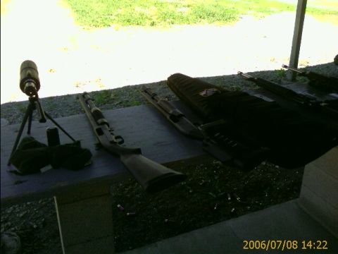 1990 Ford Bronco - A spotting scope and several shotguns are set up on a table at a shooting range, with spent shell casings visible on the ground.