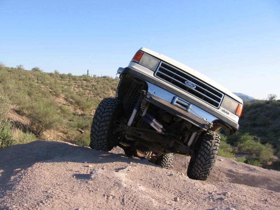 White Ford F-Series truck with lifted suspension and large tires driving off-road