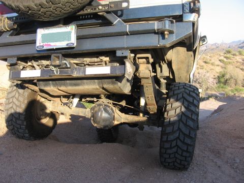 1990 Ford Bronco - The rear suspension and axle of a Ford Bronco are visible, with a spare tire mounted above the bumper.