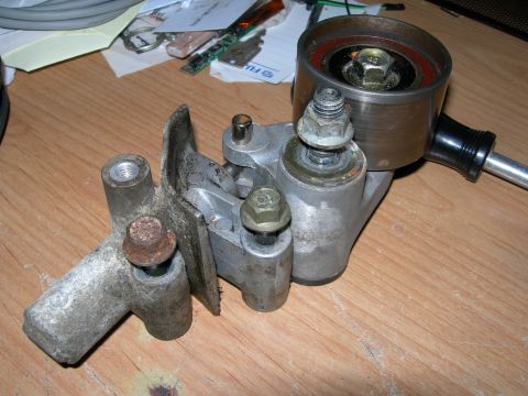 1992 Ford Taurus - A disassembled belt tensioner assembly lies on a wooden surface, with various tools and papers in the background.