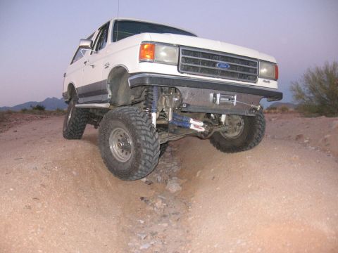 1990 Ford Bronco - This lifted Ford Bronco navigates a rough, dusty terrain with its front wheels angled.