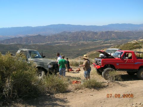 1985 Ford Bronco - A group of people gathered around two off-road vehicles on a sunny day with a scenic mountain vista.