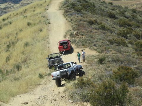 1990 Ford Bronco - Looking down a grassy ridge trail at a red Jeep, a small truck and a white 4x4 with people gathered between them.