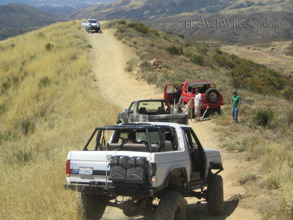 White Ford open-top 4x4 and other trucks on a grassy mountain trail
