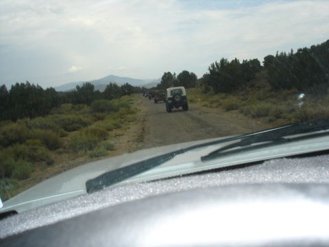 1996 Ford Bronco - A convoy of Jeeps travels on a remote dirt road under a cloudy sky.