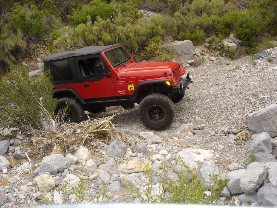 Red Jeep Wrangler with a black soft top driving on a rocky, off-road trail