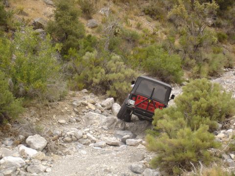 1996 Ford Bronco - A red Jeep Wrangler navigates a rocky, off-road trail with sparse vegetation.