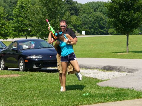 1991 Ford Probe - A black coupe with a red emblem is parked on grass while a couple plays with water guns.