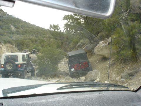 1996 Ford Bronco - Multiple Jeeps traverse a challenging, rocky mountain path, suggesting an off-road adventure.