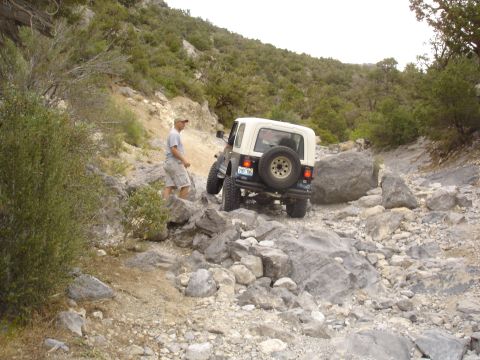1996 Ford Bronco - Jeep Wrangler tackling a difficult rocky trail with a person standing nearby.