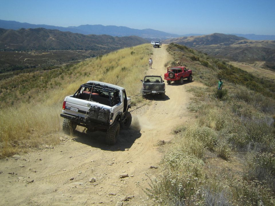 White 4x4 kicking up dust climbing a ridge trail toward other vehicles