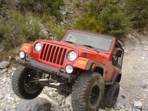 1996 Ford Bronco - A red Jeep Wrangler navigates a rocky trail, its tires gripping the uneven surface.