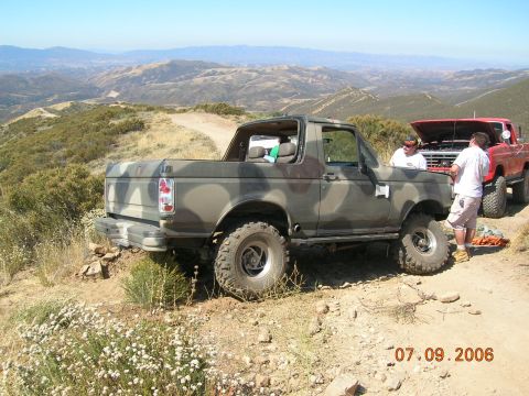 1985 Ford Bronco - Two trucks parked on a mountain trail, one is a camouflaged Ford Bronco.